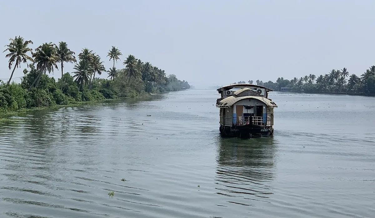 A traditional Kerala houseboat cruising a wide palm-lined backwater canal near Alleppey