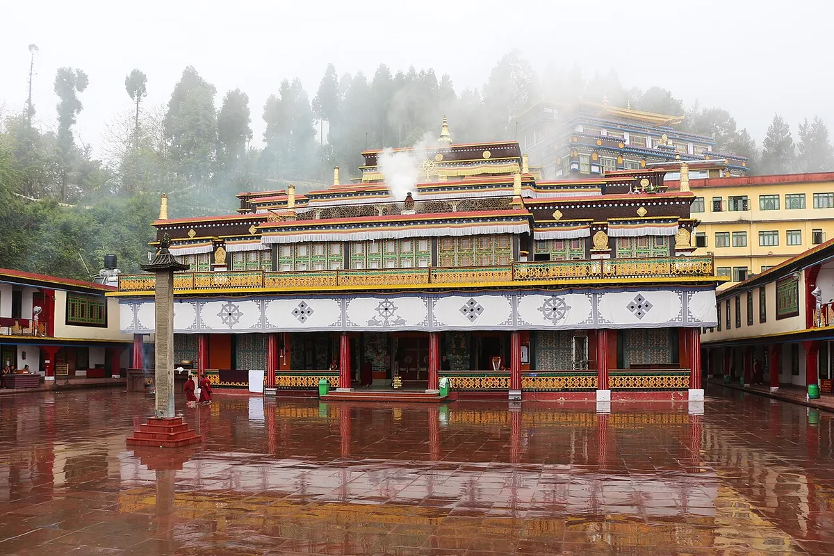 The main temple of Rumtek Monastery across its stone courtyard near Gangtok, incense smoke rising from the roof, monks in maroon robes at the edges
