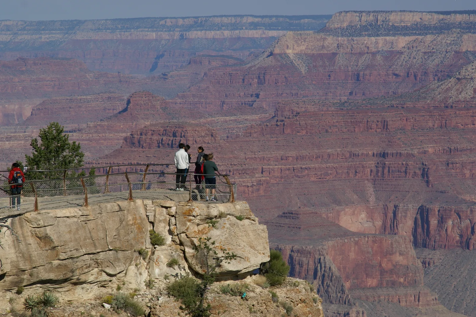 Visitors at a railed viewpoint on the South Rim, looking across the Grand Canyon's layered red and amber walls