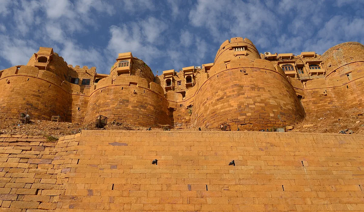 The golden sandstone bastions of Jaisalmer Fort rising above their sloped stone apron against a blue sky