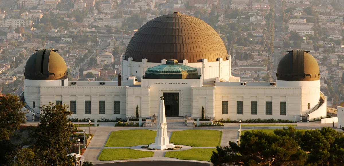 Griffith Observatory's domed white building with the Astronomers Monument on the lawn in front, the city spread out behind it