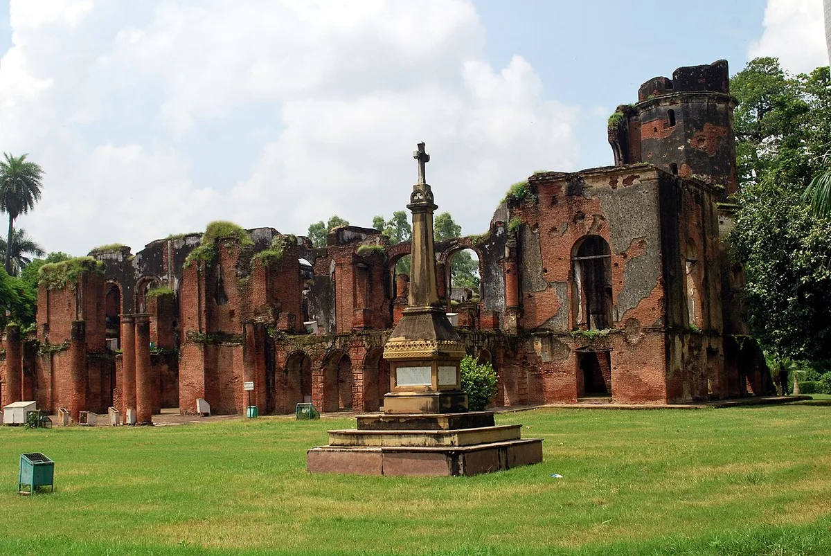 The ruined main building of the Lucknow Residency across its lawns, with the memorial cross in the foreground