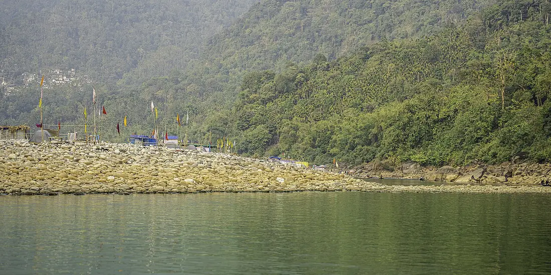 The Umngot River at Dawki in Meghalaya, its stony bank and forested hills above calm green water