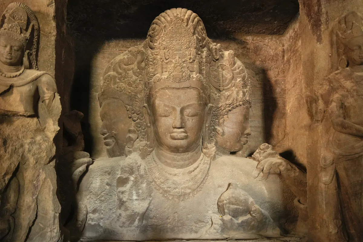 The three-faced Mahesa-murti, known as the Trimurti, carved in stone inside Cave 1 at Elephanta, flanked by guardian figures