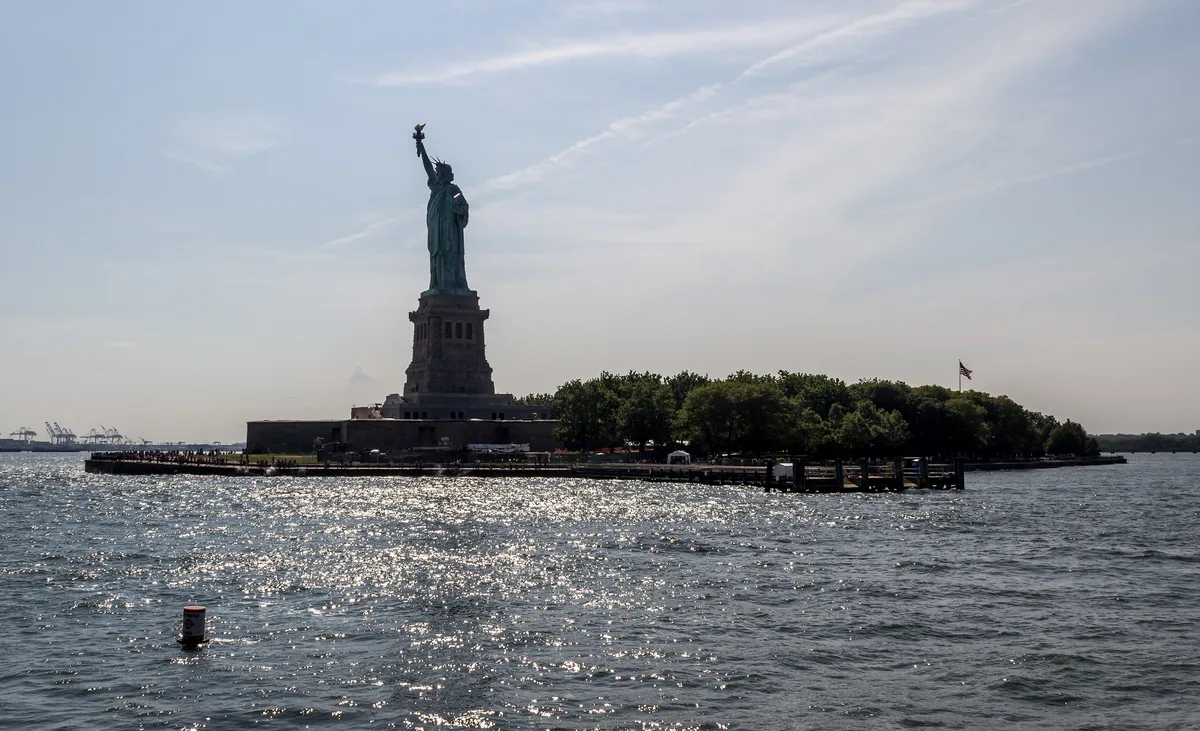 The Statue of Liberty on its pedestal, seen from the harbour side against a clear sky