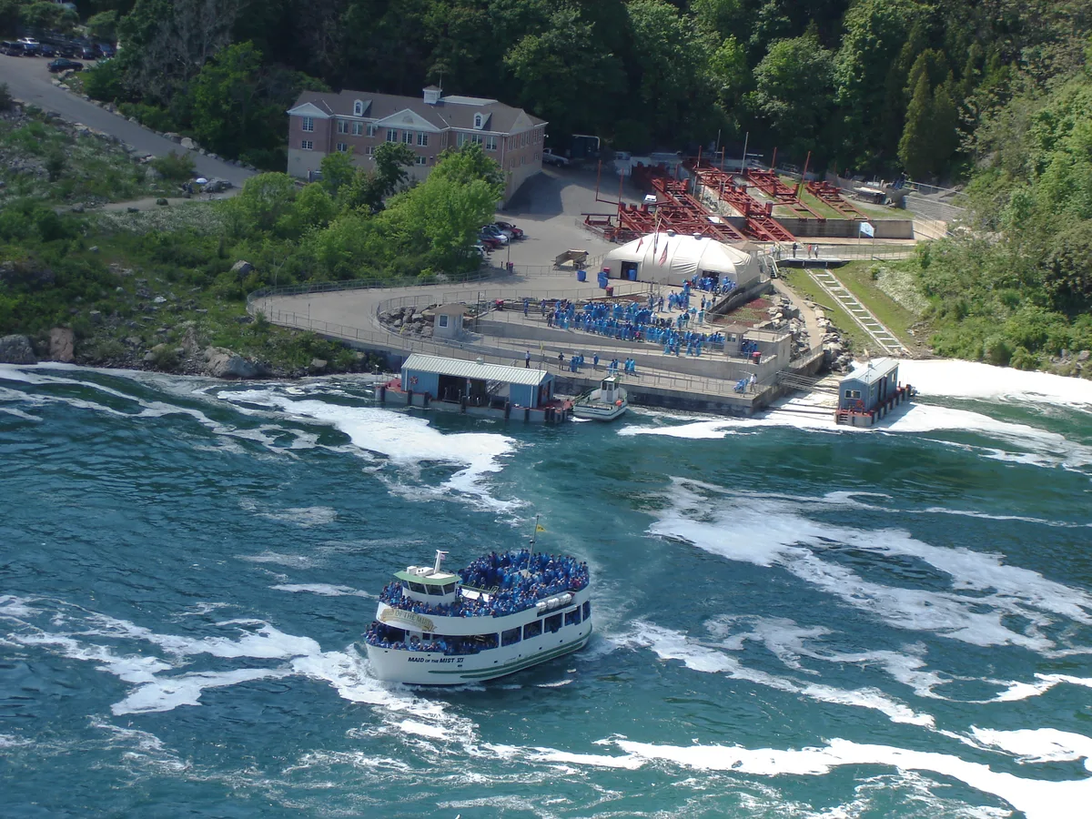 A Maid of the Mist boat crowded with passengers in blue ponchos pulling away from the landing, where the next crowd waits in the same blue