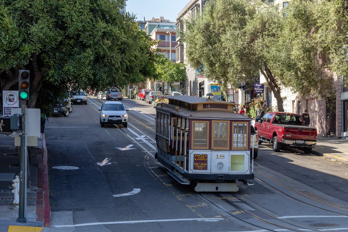 The rear of a Powell and Hyde cable car climbing a tree-lined San Francisco hill street