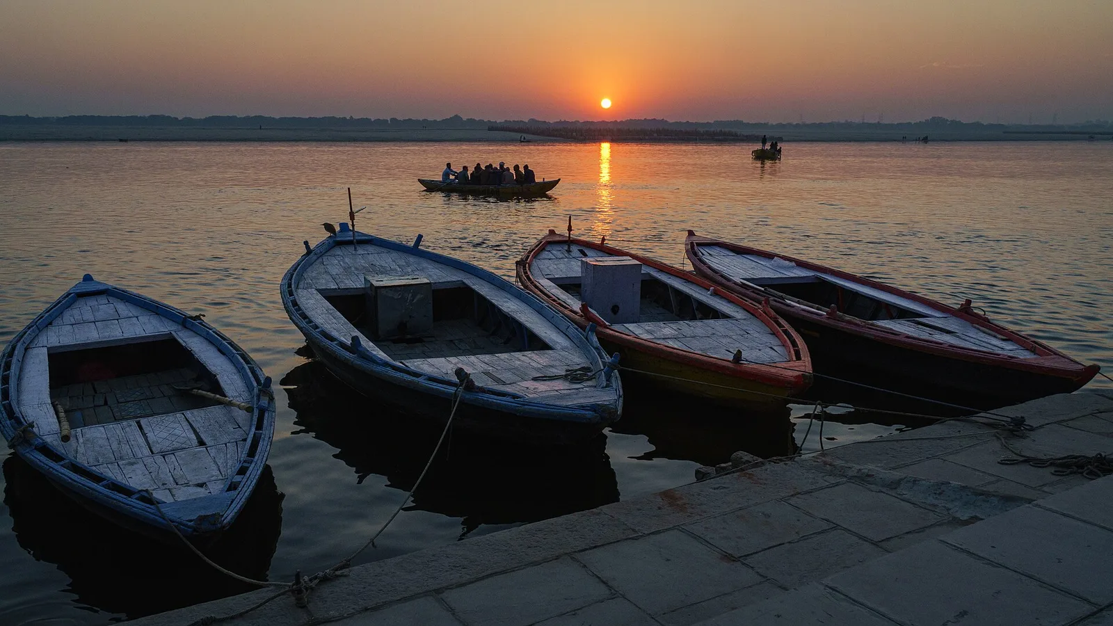 Rowing boats moored on the Ganga at Varanasi as the sun rises over the river